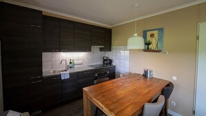 Een moderne keuken met donkere kasten, een houten eettafel en een hanglamp.