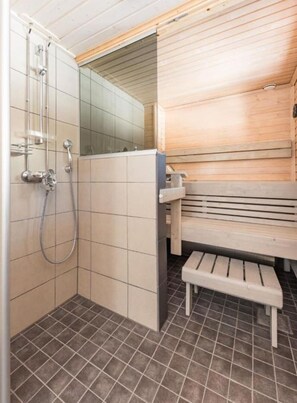 A sauna room with a bench, a shower area with a glass door, and tiled flooring. - Onnela 2 Chalet | Private Sauna & Fireplace | Ruka (Kuusamo)