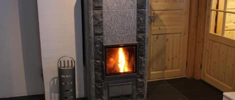 A stone fireplace with a visible fire, a metal ashtray, and a wooden door in the background.