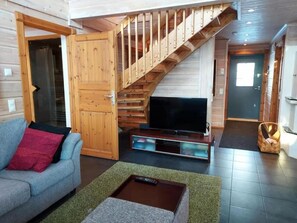 Ein Wohnzimmer mit einer Couch, einem Fernseher, einer Holztreppe und einer Tür zu einem anderen Raum.