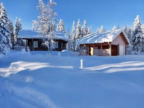 Eine Hütte mit schneebedecktem Dach und Holzfassade, umgeben von schneebedeckten Bäumen.