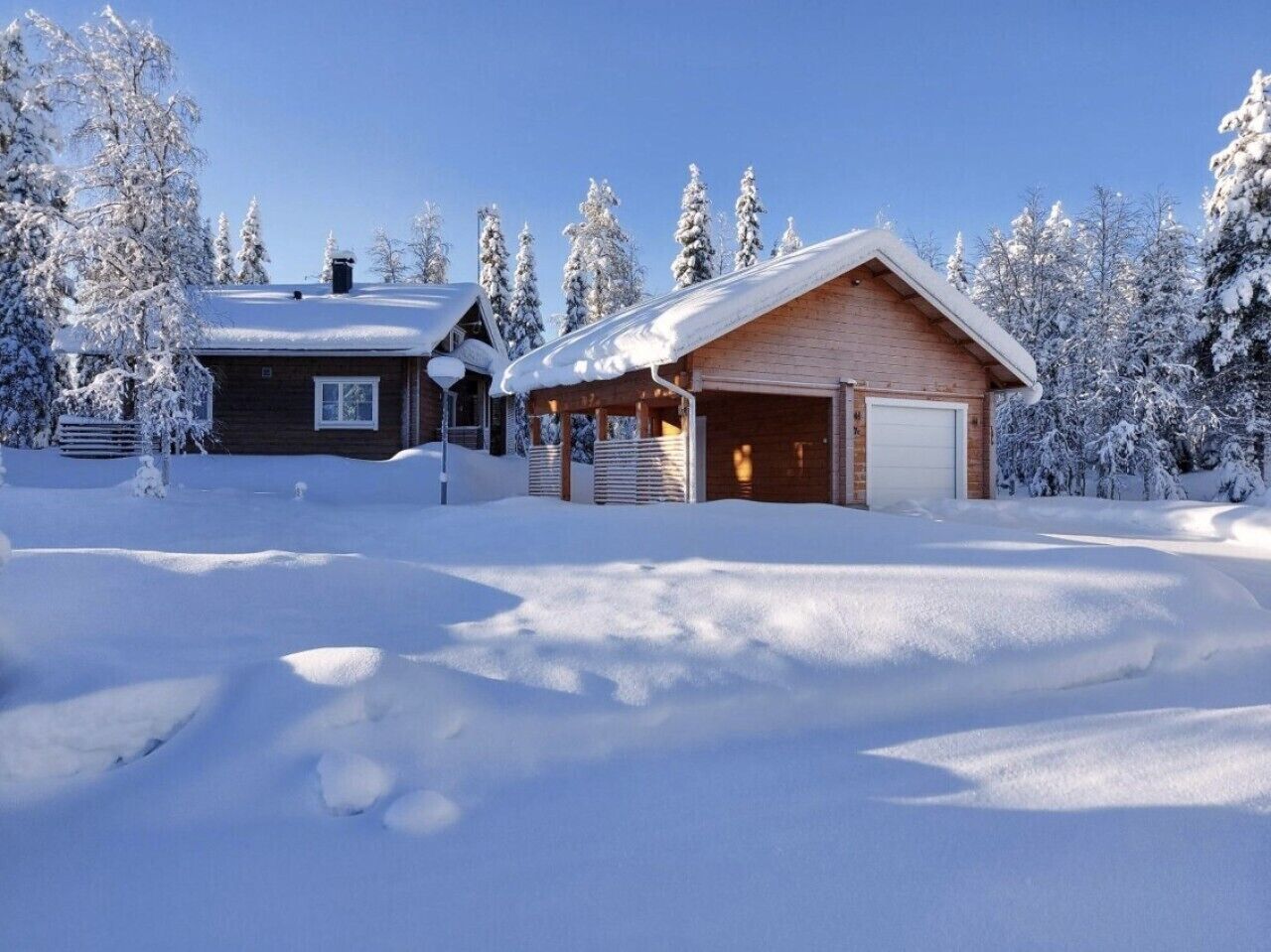 Une cabane en bois avec un garage et un bâtiment séparé, le tout entouré d’arbres couverts de neige.
