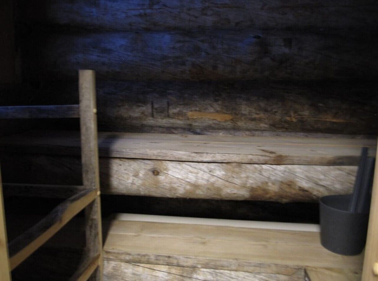 A wooden interior with a metal ladder and a black trash bin.