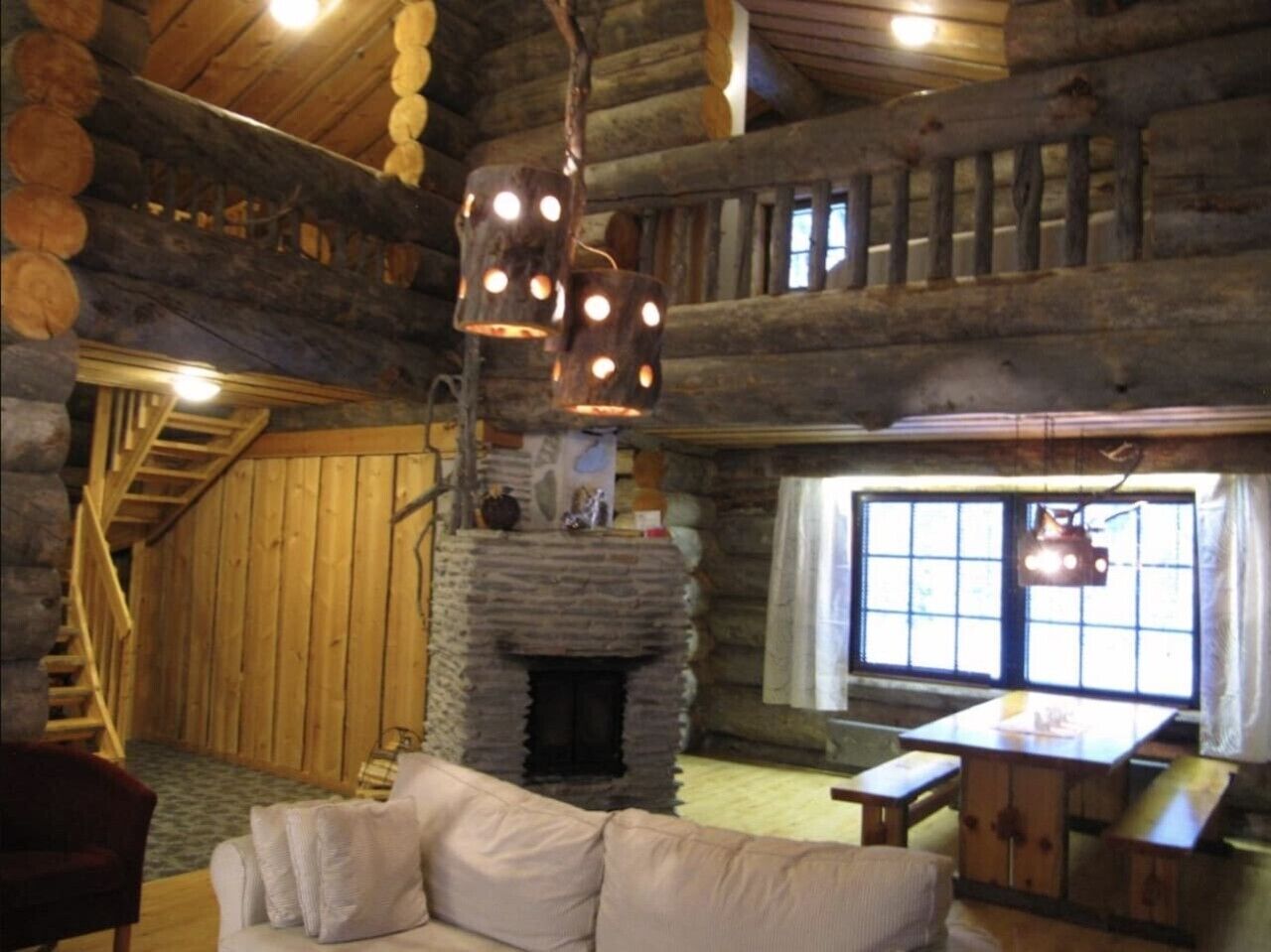 A log cabin interior with a stone fireplace, wooden staircase, and a sofa.
