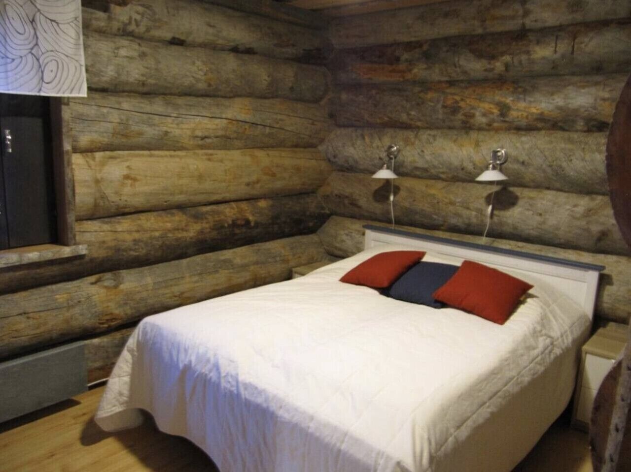 A log cabin-style room with a bed, two bedside lamps, and a window.