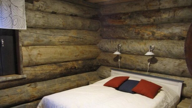 Quarto em estilo cabana de madeira, com uma cama, duas luminárias de cabeceira e uma janela.