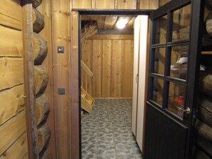 Un couloir intérieur aux murs en bois, avec une porte donnant sur une pièce.