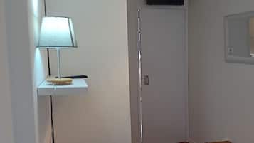 Une chambre à coucher avec un lit, une lampe de chevet, un téléviseur fixé au mur et un petit tabouret en bois.