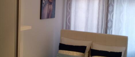 Un dormitorio con una cama, una lámpara colgante, un cuadro en la pared y una ventana con cortinas.
