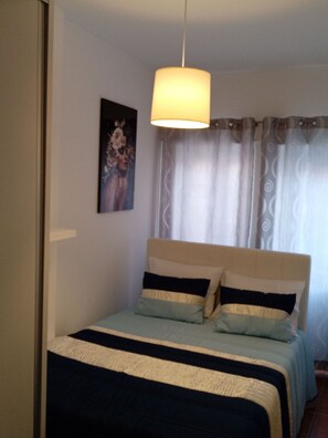 A bedroom with a bed, a hanging light fixture, a painting on the wall, and a window with curtains. - Chalas Bedroom Nazaré (Nazaré)
