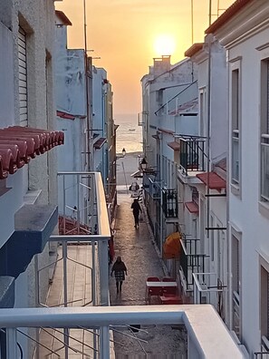 A narrow street with buildings on either side, leading towards the sea. - Chalas Bedroom Nazaré (Nazaré)