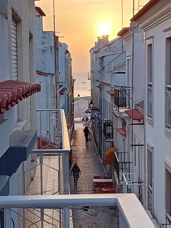 A narrow street with buildings on either side, leading towards the sea. - Chalas Bedroom Nazaré (Nazaré)