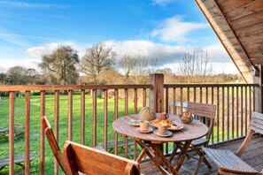 A wooden deck with a round table and chairs, a bench, and a view of a grassy field and trees. - Peaceful Oswestry Canalside Apartment (Oswestry)