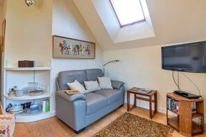 Ein Wohnzimmer mit grauem Sofa, Flachbildfernseher, Bücherregal und Dachfenster.