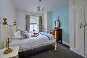A bedroom with a bed, bedside table, lamp, dresser, mirror, and a window with curtains. - Countryside Retreat Opposite Pub (Betws-Y-Coed)