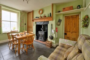 A cozy living room with a fireplace, a dining area with wooden chairs, and a sofa. - Countryside Retreat Opposite Pub (Betws-Y-Coed)