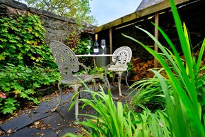An outdoor seating area with two ornate metal chairs and a table, surrounded by greenery and a stone wall. - Countryside Retreat Opposite Pub (Betws-Y-Coed)