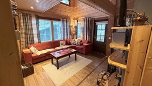 A cozy living room with a red sofa, a wooden coffee table, and a fireplace. - Rukasoihtu A | 2BR Cabin with Sauna & Fireplace (Kuusamo)
