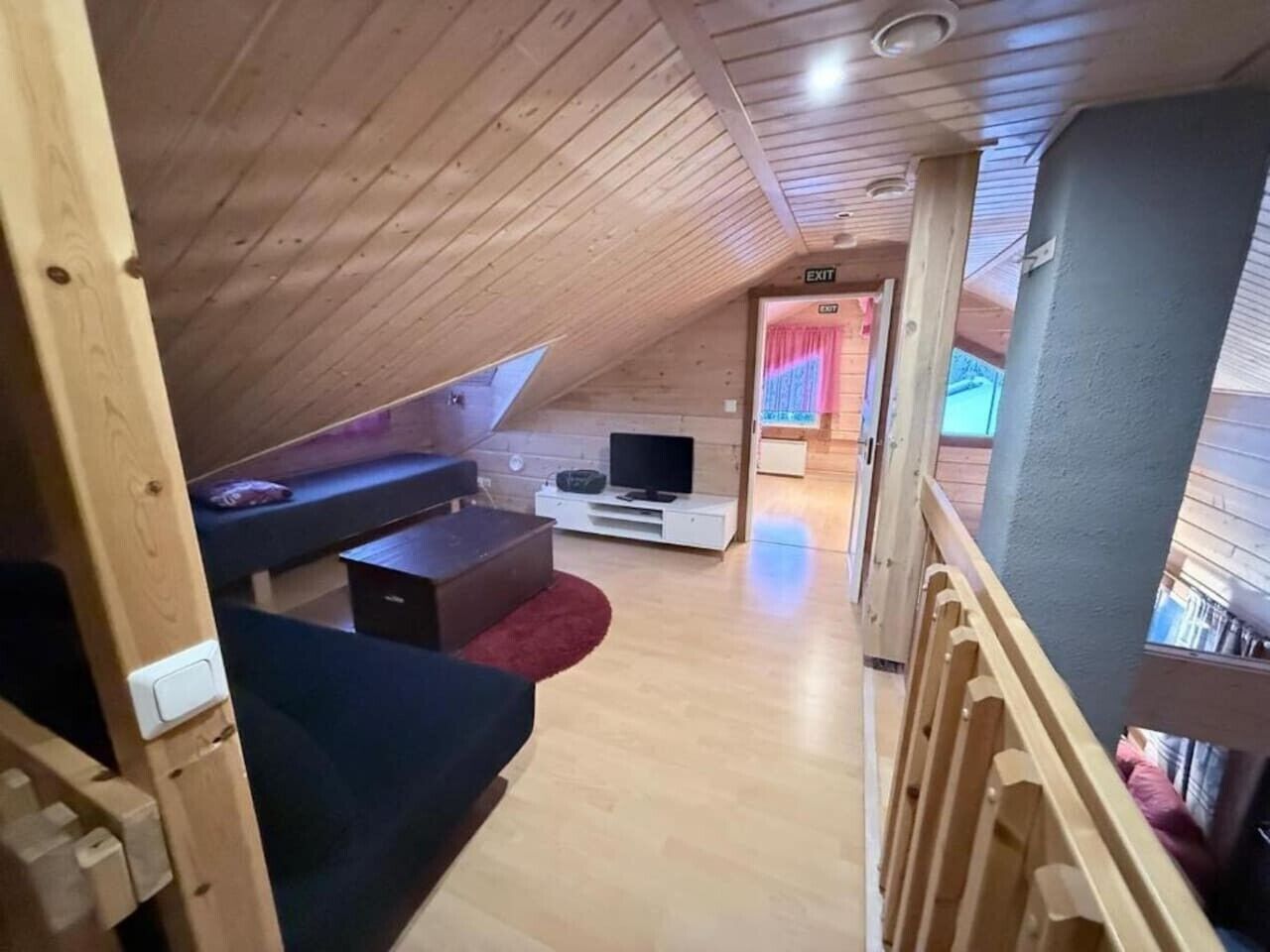 An attic bedroom with a wooden ceiling, a TV, a sofa, and a small table.