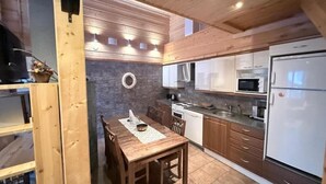 A compact kitchen with wooden cabinets, a dining table, and a built-in oven. - Rukasoihtu A | 2BR Cabin with Sauna & Fireplace (Kuusamo)