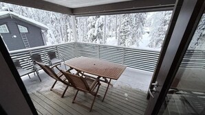 A covered outdoor area with a table and chairs, a view of a house and snow-covered trees. - Rukasoihtu A | 2BR Cabin with Sauna & Fireplace (Kuusamo)