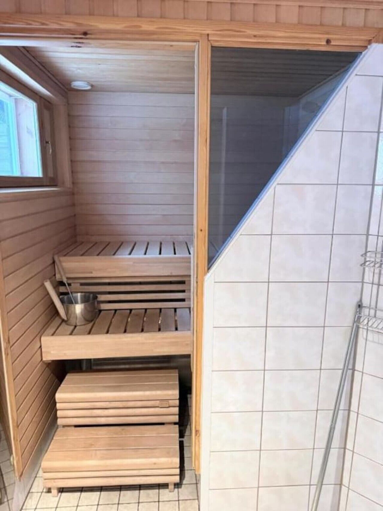 Een sauna met houten banken, een metalen emmer en een glazen deur.