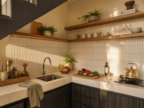 A modern kitchen with a built-in sink, wooden shelves, and a variety of kitchenware. - Villa Gaudi II (Kabupaten Badung)