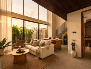 A modern living room with a sofa, coffee table, and potted plants. There is a staircase leading to an upper level. - Villa Gaudi II (Kabupaten Badung)