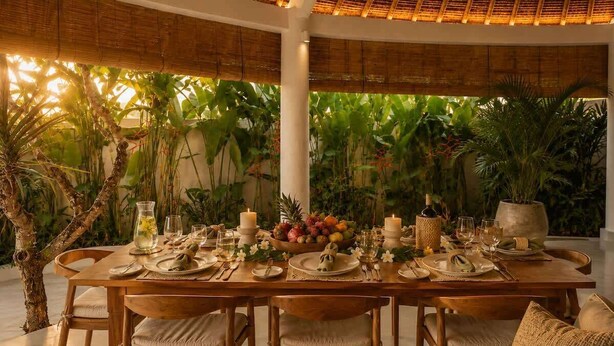 A dining table set for six with candles, fruit, and glassware, surrounded by chairs and plants. - Villa Juma (Kabupaten Badung)
