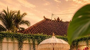 A poolside area with two lounge chairs, a decorative umbrella, and a wall adorned with hanging plants and flowers. - Villa Juma (Kabupaten Badung)