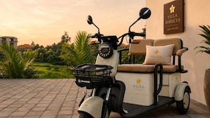 A stationary electric scooter with a seat and a basket, parked on a paved surface with a building in the background. - Villa Hibiscus I (Kabupaten Badung)
