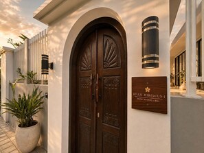 A villa entrance with a large wooden door, a signboard, and a potted plant. - Villa Hibiscus I (Kabupaten Badung)