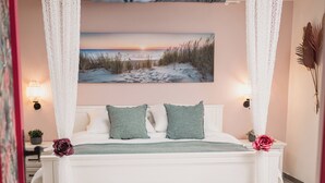 Quarto com cama, um banco, uma pintura e uma mesinha de cabeceira.