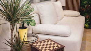 Uma sala de estar moderna com um sofá branco, uma pequena mesa lateral de madeira com um tabuleiro de xadrez e uma planta em vaso.