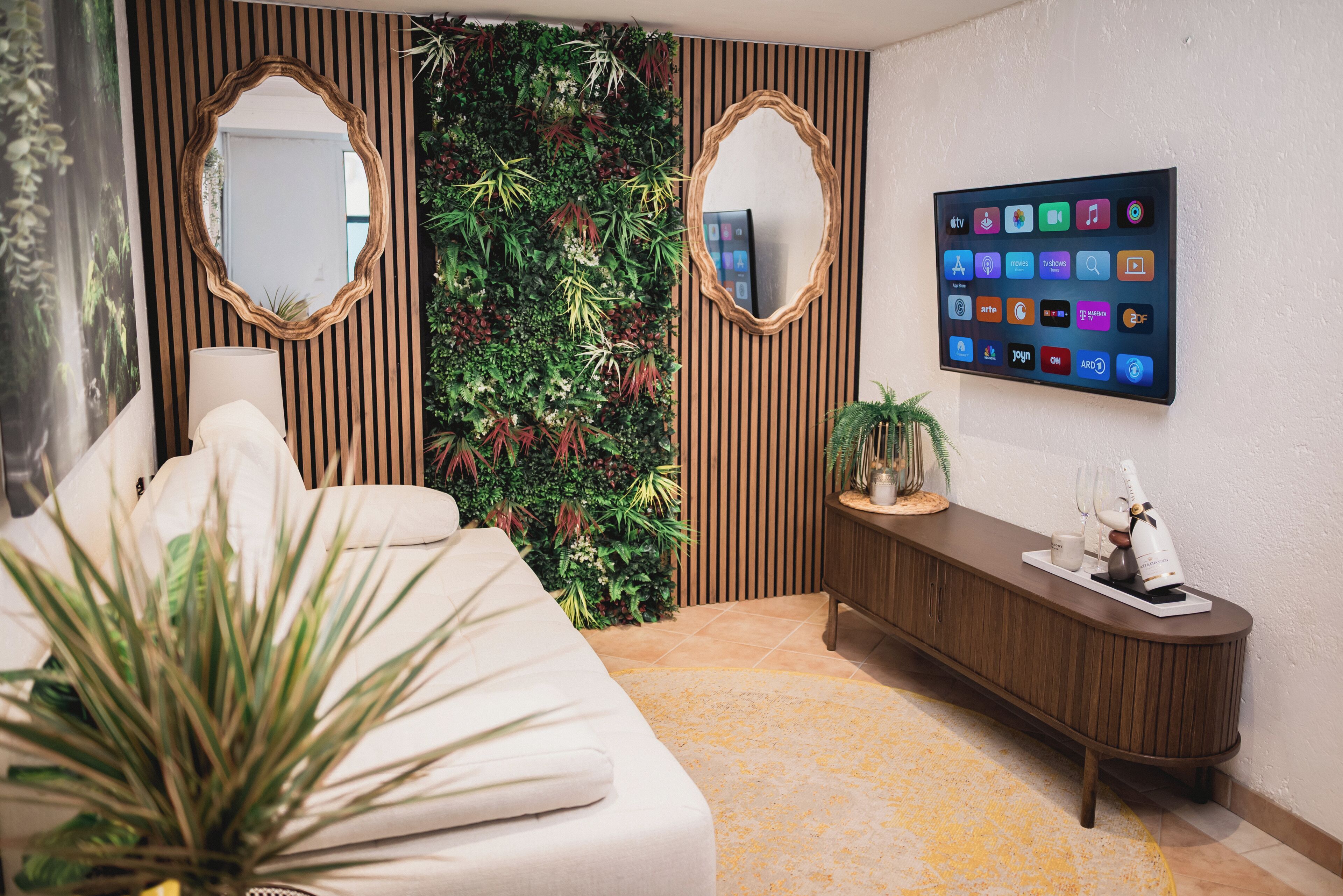 A modern bedroom with a bed, a console table, a TV, and a decorative plant wall.