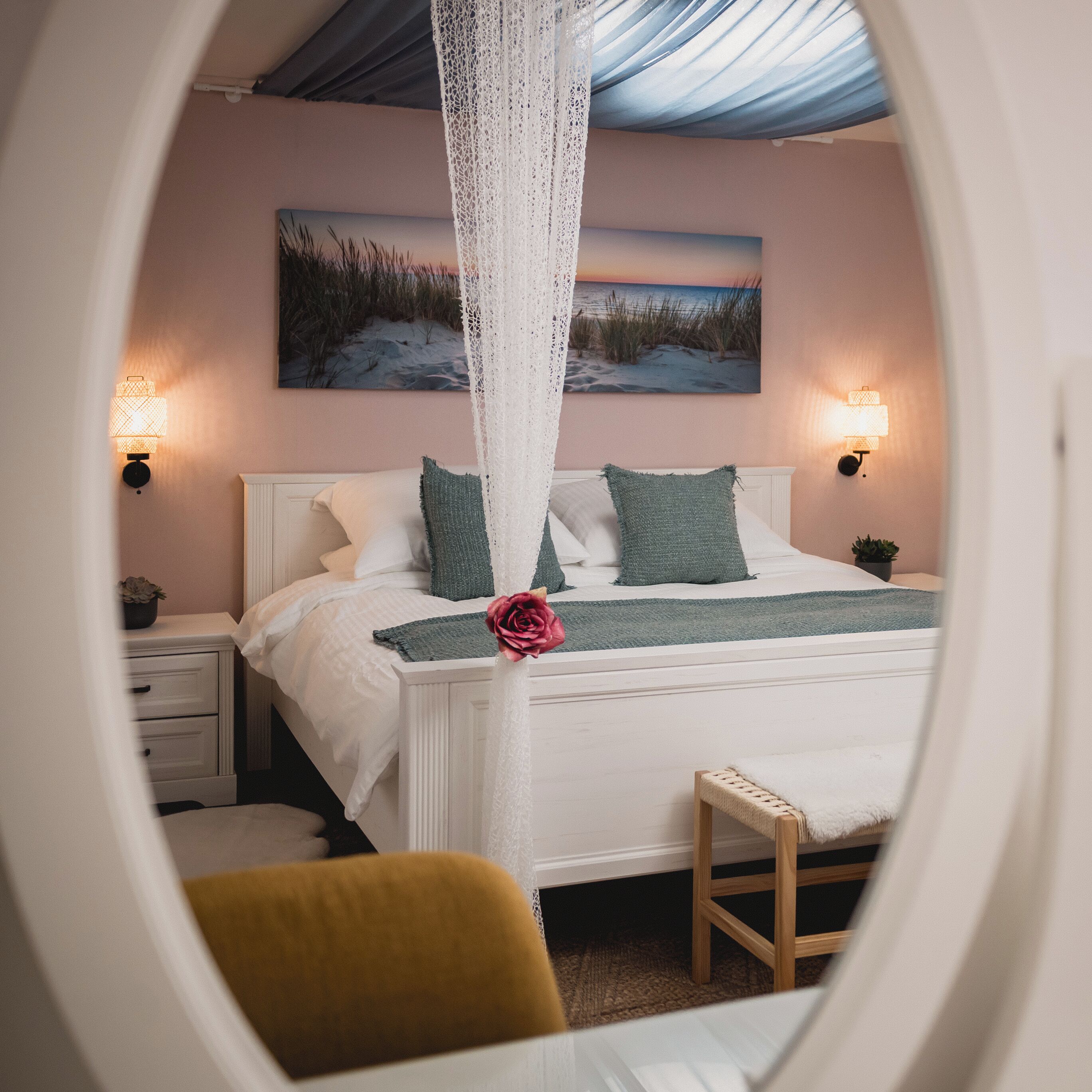 Ein Schlafzimmer mit einem Bett, Nachttischlampen, einem Gemälde und Blick durch ein Fenster.