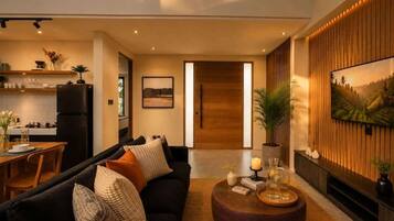 A modern living room with a black sofa, a round coffee table, and a TV mounted on the wall.