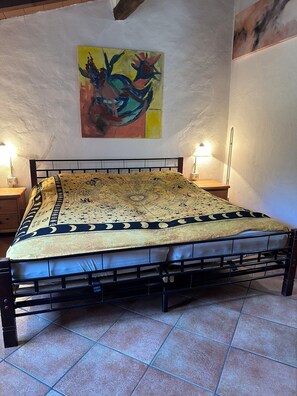 A bedroom with a bed, a nightstand, a lamp, and a painting on the wall. - Cozy vacation rental in a quiet location in the heart of a nature reserve, with a pool (Sassetta)
