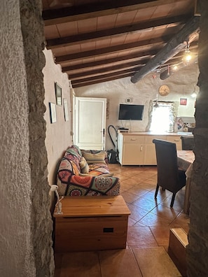 Ein rustikales Interieur mit einer Couch, einer Holzkiste, einem Fliesenboden und einer Küchenzeile mit einem Fernseher.