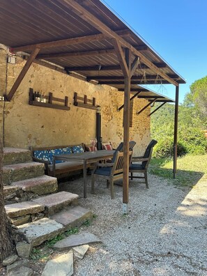 Ein rustikaler Sitzbereich im Freien mit einer Steinmauer, Holzbanken und einem Kiesweg.