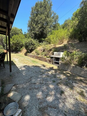 Un patio de grava con un banco de piedra, una parrilla y un espacio cubierto con una mesa y sillas.