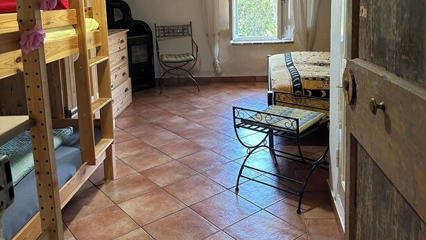 Una habitación rústica con un armario de madera, una cama, una silla y una ventana con cortinas.