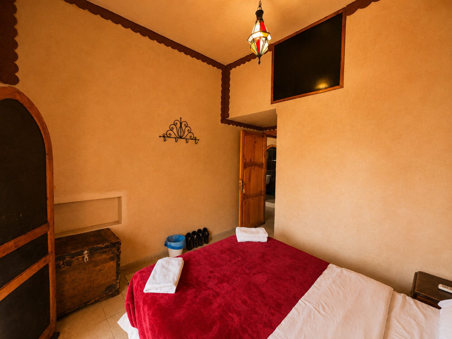 A bedroom with a bed, a chest of drawers, a wardrobe, a hanging light fixture, and a window.