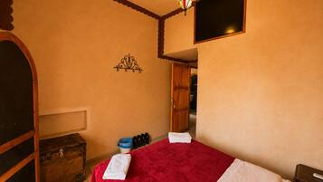 A bedroom with a bed, a chest of drawers, a wardrobe, a hanging light fixture, and a window.