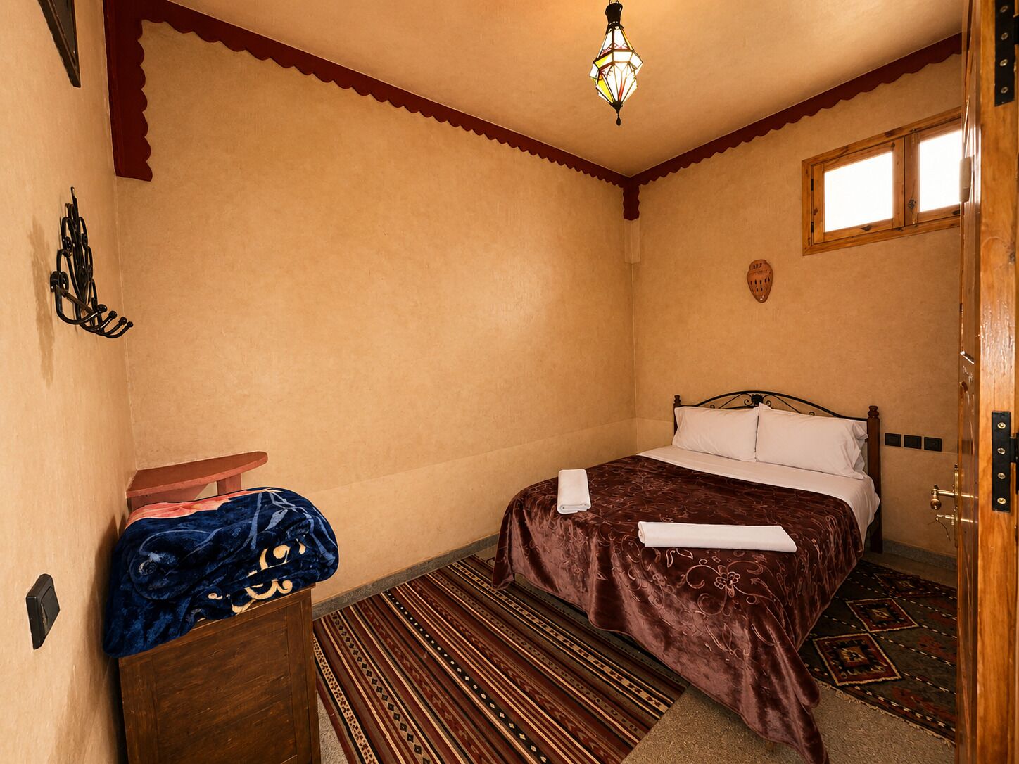 A bedroom with a bed, a wooden dresser, a patterned rug, and a decorative wall piece.