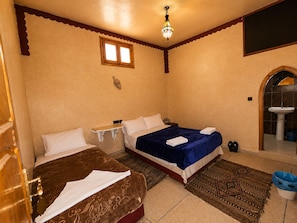 Una habitación con dos camas, una mesita, una lámpara colgante, una ventana y un baño con lavamanos.