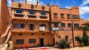 A multi-story building with balconies, a restaurant sign, and potted plants. - Auberge Restaurant Zahra (Ait Sedrate Jbel El Soufla)