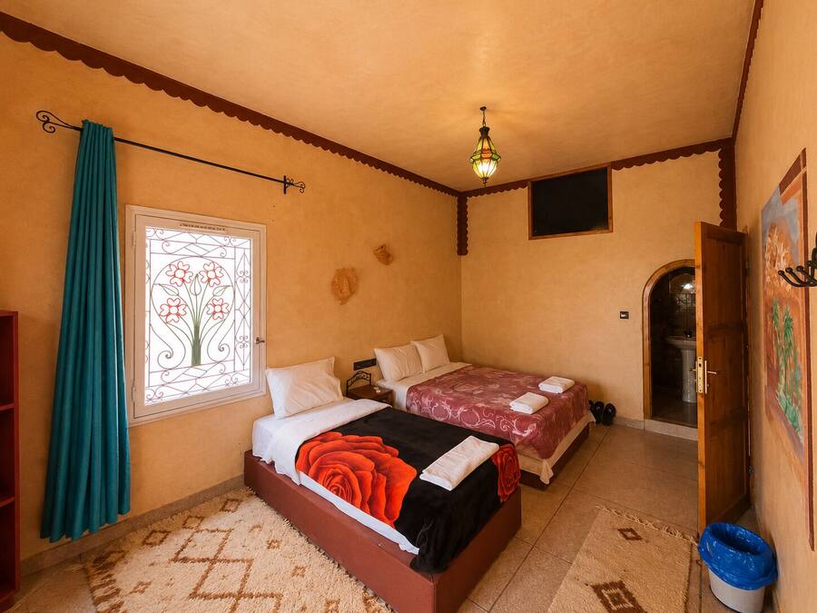 A bedroom with two beds, a window with a decorative design, a ceiling light, and a door leading to a bathroom.
