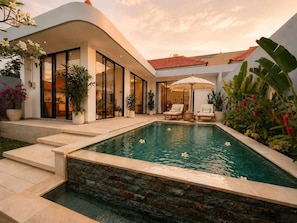 Ein modernes Haus mit Swimmingpool, Sitzgelegenheiten im Freien und üppiger Bepflanzung.