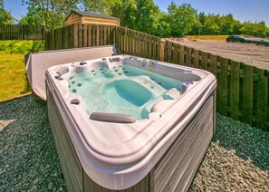 A hot tub with a wooden deck surrounding it, a wooden fence, and a shed in the background.